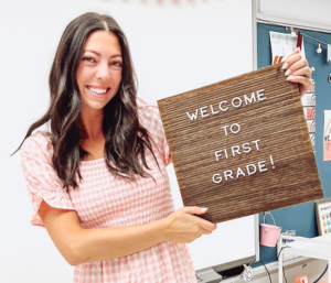 Picture of Ms. Justine Faucett with Welcome to 1st grade sign