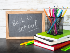 Small framed chalkboard reading "Back to school" next to a stack of books and a pencil holder filled with colored pencils.